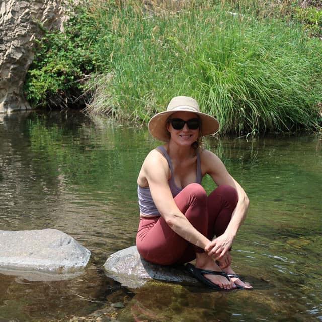 Chrissy Gunn smiling on a rock near a body of water