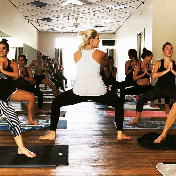 a group of students with their instructor are in a standing pose with their hands set in a prayer position