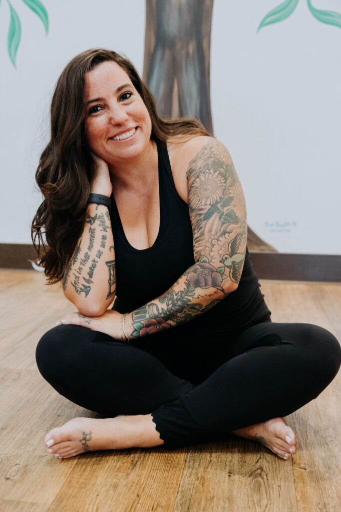 SARA RODRIGUEZ smiling indoors in a cross legged seated position