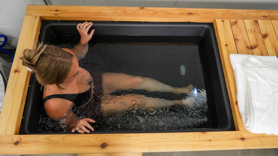 A woman immersed in a cold plunge bath with a towel nearby