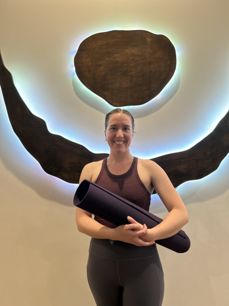 Ashley Kiefer holding her yoga mat in front of the business logo